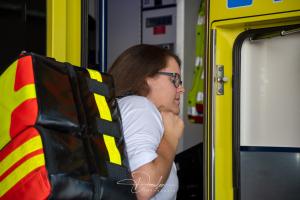 Eine Person trägt eine große, bunte Rettungstasche auf dem Rücken und steht an der Tür eines Rettungswagens.