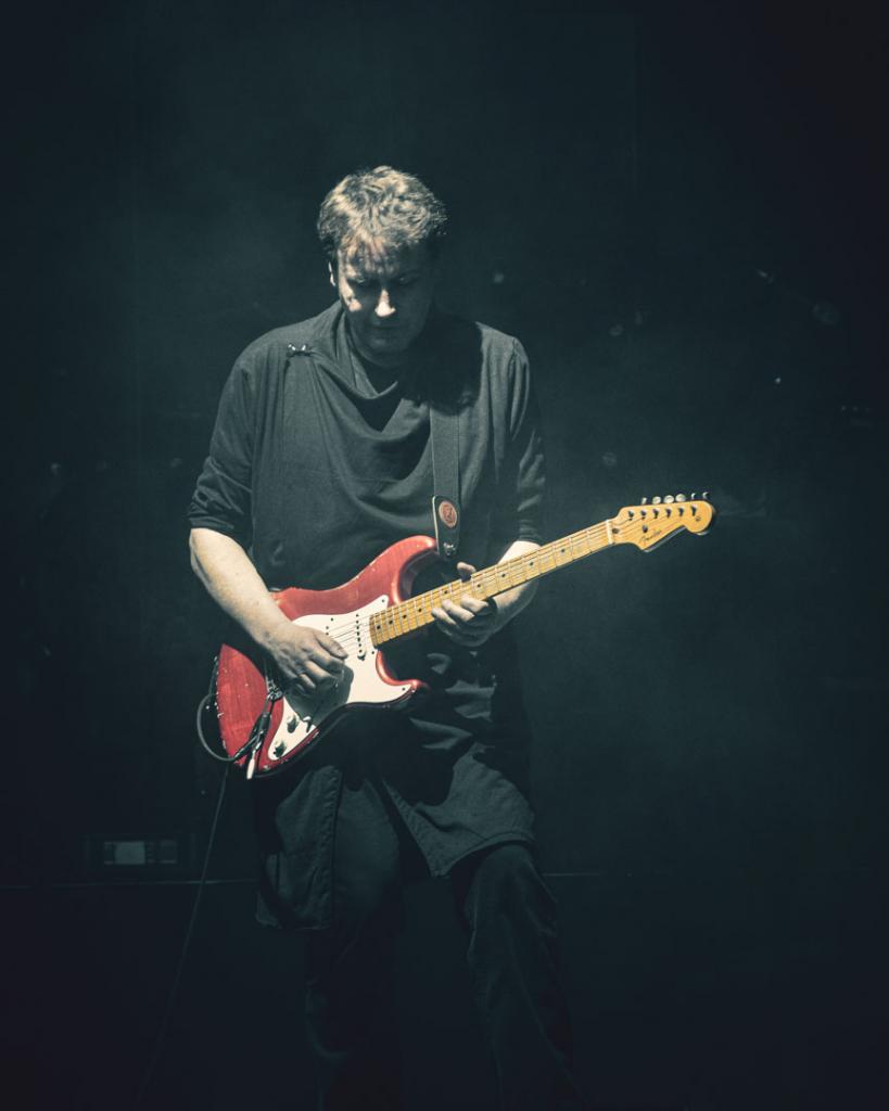 Event Fotografie 3 Person spielt E-Gitarre auf einer Bühne im schummrigen Licht.