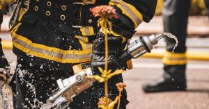 Feuerwehrmann in Schutzkleidung mit Feuerwehrschlauch, aus dem Wasser spritzt.