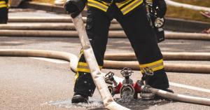 Ein Feuerwehrmann in Schutzkleidung steht auf einer Straße mit mehreren Feuerwehrschläuchen.