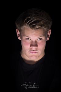 Porträt eines jungen Mannes vor schwarzem Hintergrund, ausdrucksstark beleuchtet.
