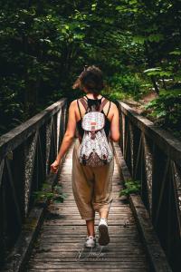 Frau mit Rucksack geht über eine Holzbrücke im Wald.