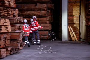 Rettungsteam mit Hund in einer Holzlagerhalle.