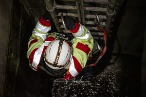 Ein Rettungskletterer in reflektierender Kleidung und Helm klettert eine Metallleiter hinab, gesichert mit einem Karabiner.