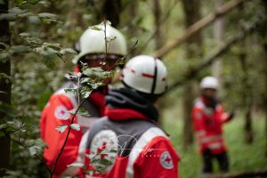 Personen in roten Rettungsdienst-Uniformen und Helmen im Wald.