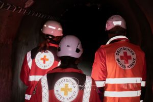 Drei Personen in Schutzhelmen und Westen des Deutschen Roten Kreuzes in einem dunklen Tunnel.