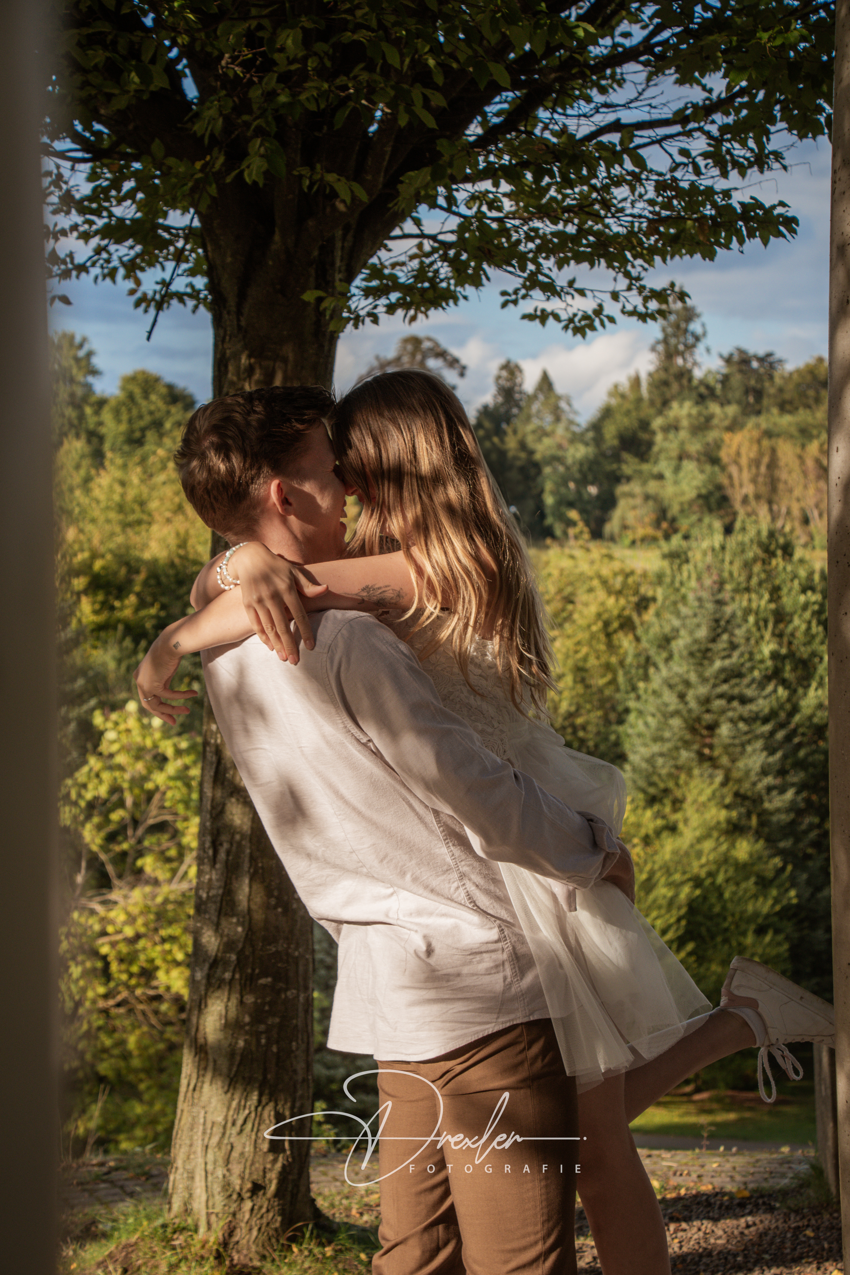 Ein Paar umarmt sich innig unter einem Baum in einer natürlichen Umgebung.