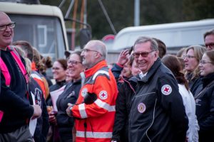 Eine Gruppe von Menschen in Rettungsdienstkleidung und mit Rotkreuz-Logos steht beisammen und lächelt.