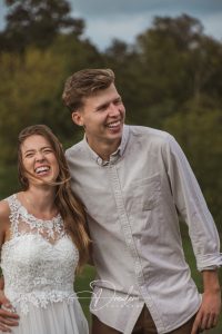 Ein lachendes Paar steht im Freien; der Mann trägt ein cremefarbenes Hemd, die Frau ein Spitzenkleid.